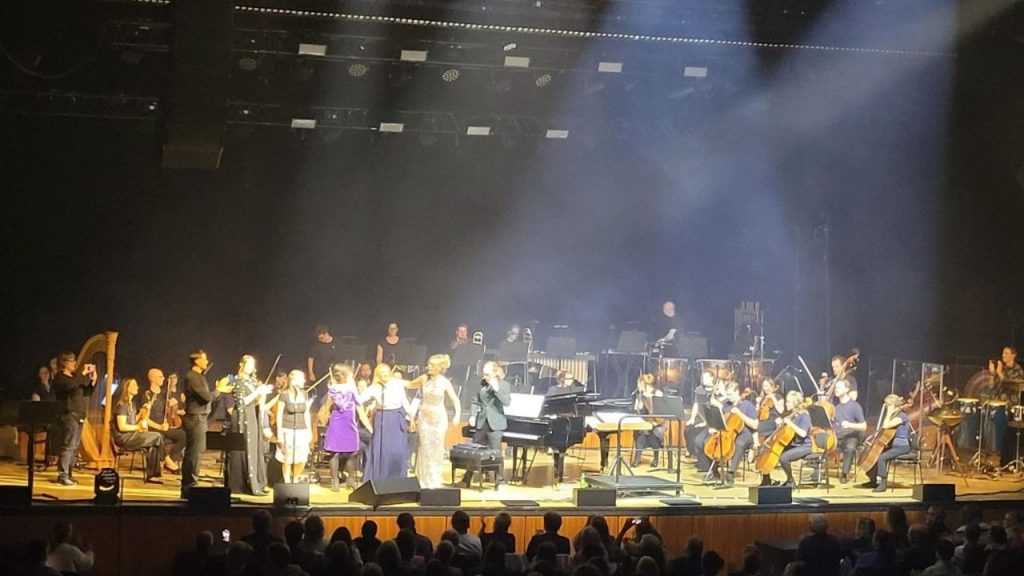 Drei ausgewählte Sängerinnen gemeinsam mit weiteren Mitwirkenden und dem Orchester auf der Bühne bei „Kosmos und Orchester“ in Stuttgart 2026